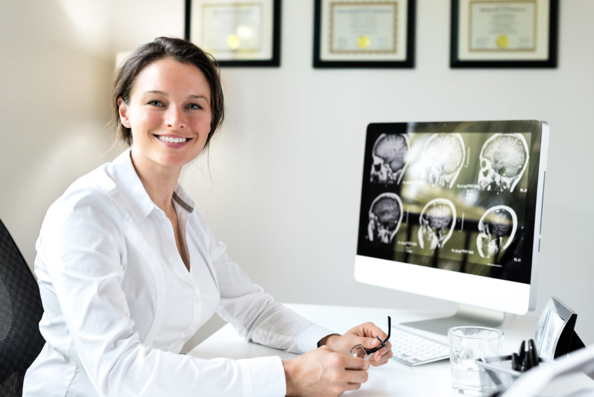 doctor sitting at desk with framed diplomas on wall behind her
