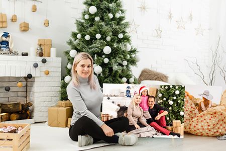 women sitting in front of Christmas tree showing her personalized holiday photo gift
